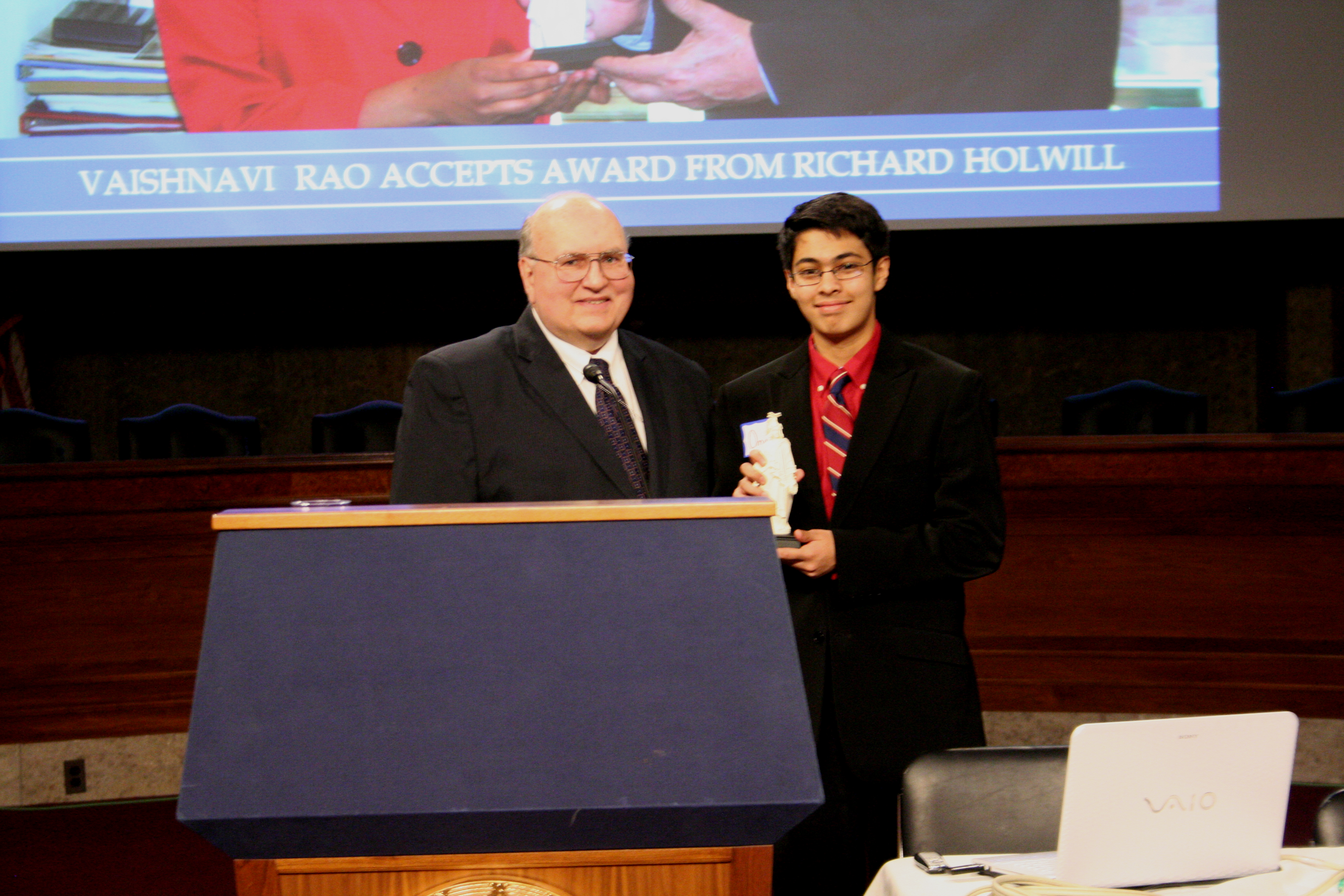 Omar Qureshi accepts the first place award in the Junior Division of the 2012 student essay contest from Society Vice President Don Kennon at the annual symposium on May 3, 2013, in the auditorium in the Dirksen Senate Office Building.